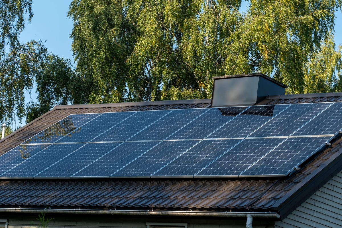 Solar panels on home roof against blue sky and trees